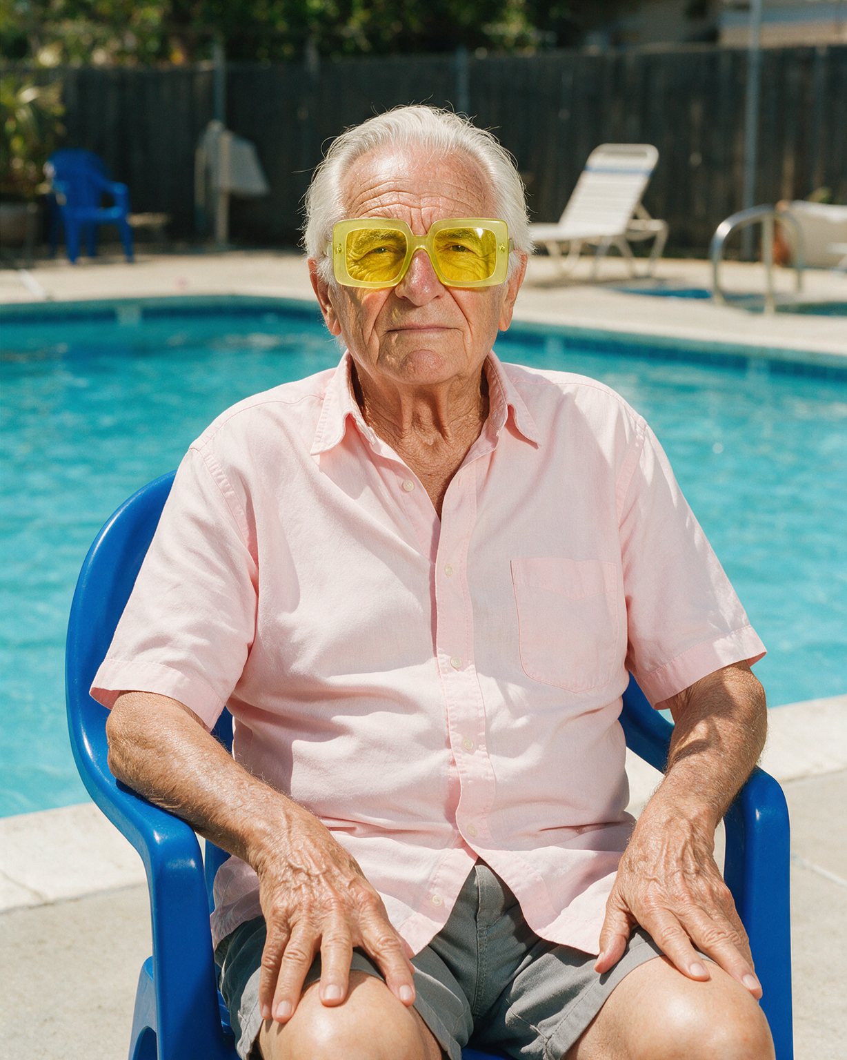 Elderly man in lemon-yellow sunglasses on a cobalt chair by a pool
